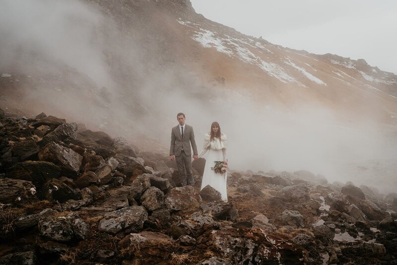 Bride and groom hold hands on a misty, moody, rocky trail during their elopement in Iceland. 
