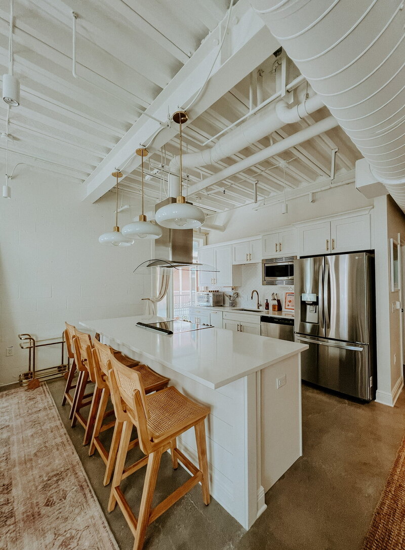 white kitchen with rattan bar stools and stainless steel appliances