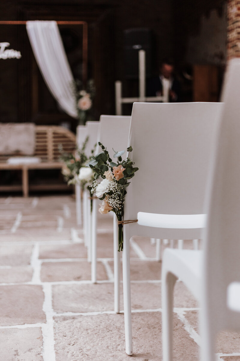 Bloemen aan de stoelen voor een ceremonie in een orangerie.