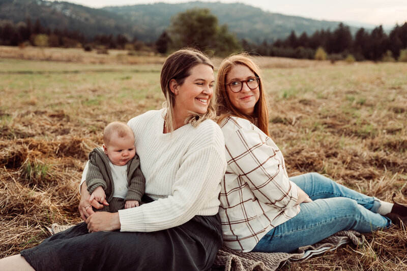Family sitting in bed laughing with a newborn and toddler