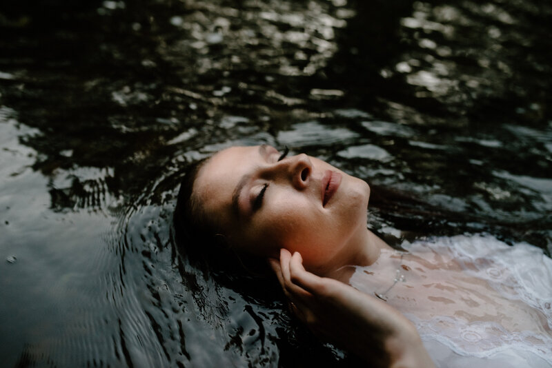 woman wearing white dress laying in water peacefully tucking hair behind ear with eyes closed