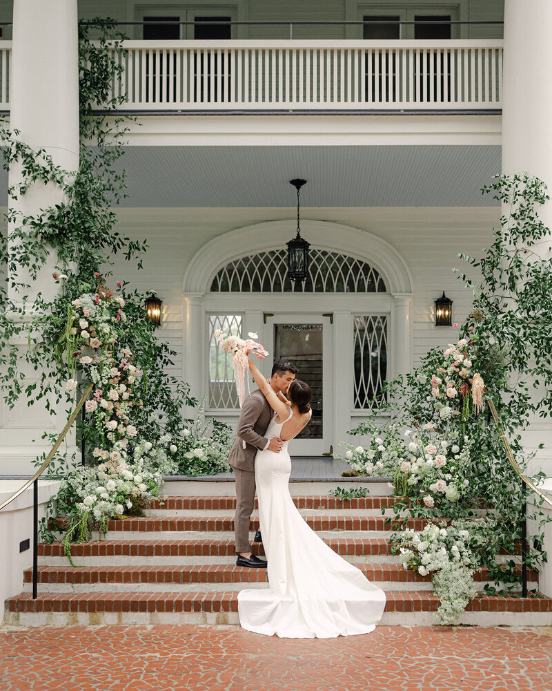 Bride and Groom kiss on stair filled with lush florals in Charleston.