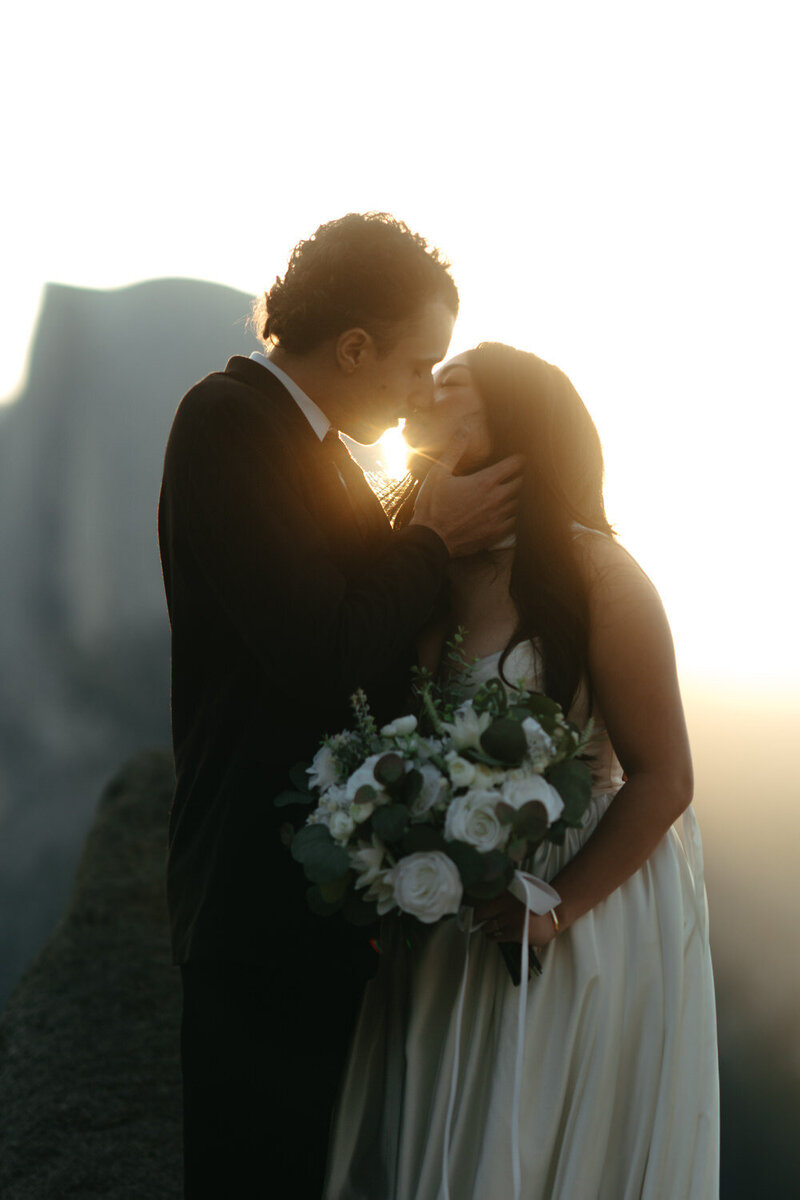 Bride and groom kissing during their Yosemite elopement with a sun ray right between their heads