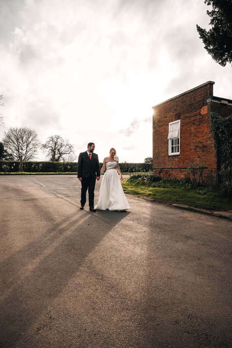 Married couple hold hands whilst walking past building smiling