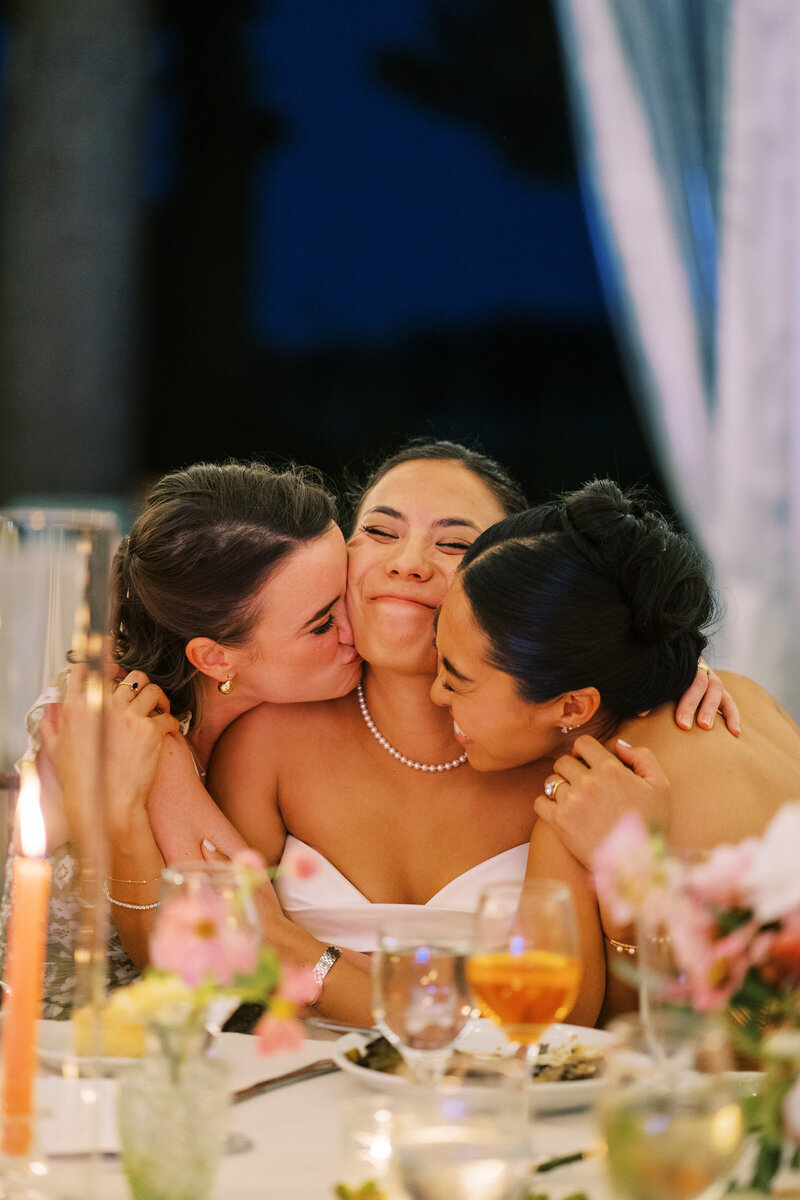 Maids of honor hug bride at her seat at Glen Foerd Estate in Philadelphia, PA