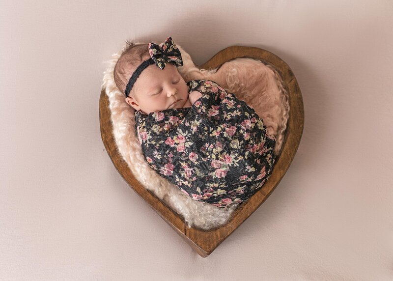 Twin baby girls sleeps in pink swaddles on a bed of pink flowers