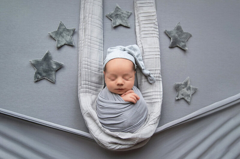 newborn baby boy wrapped in grey with a grey sleepy hat with stars around for his Burlington newborn photos.