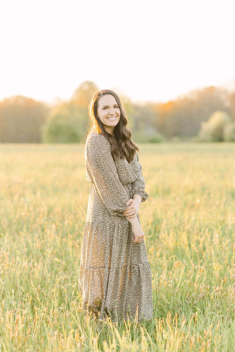 Corinne Isabelle, who specializes in Boston newborn photography, standing in a field during golden hour