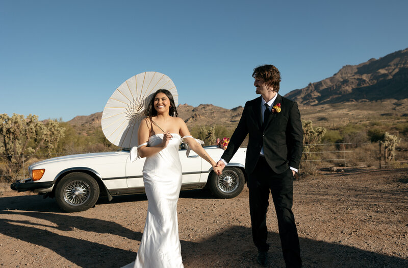 Elegant Bride and Groom walking in front of vintage car by Superstition Mountain 