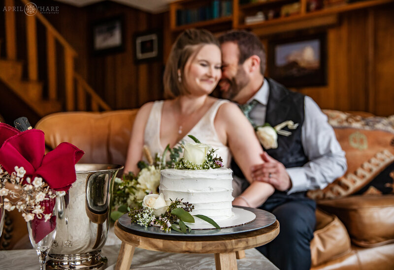 Couple Sit on the Couch with their Wedding Cake at Romantic Riversong Inn on their Wedding Day in Estes Park