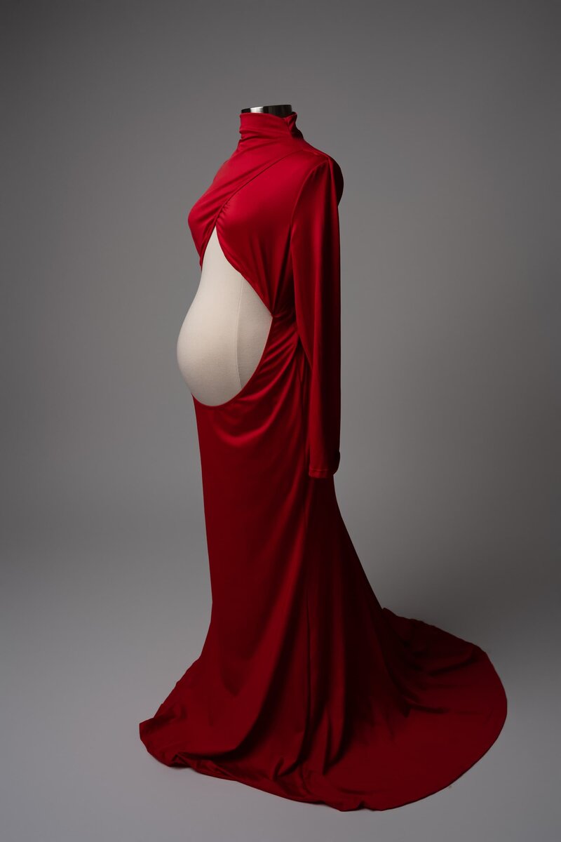 Studio maternity dress in deep red with draped sleeves and cutout belly – photographed against gray backdrop
