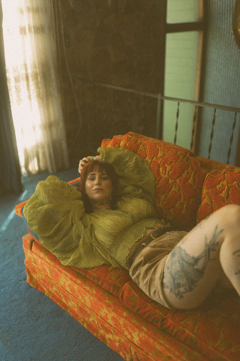 A red headed woman in a stylish green top laying on a vintage sofa. 