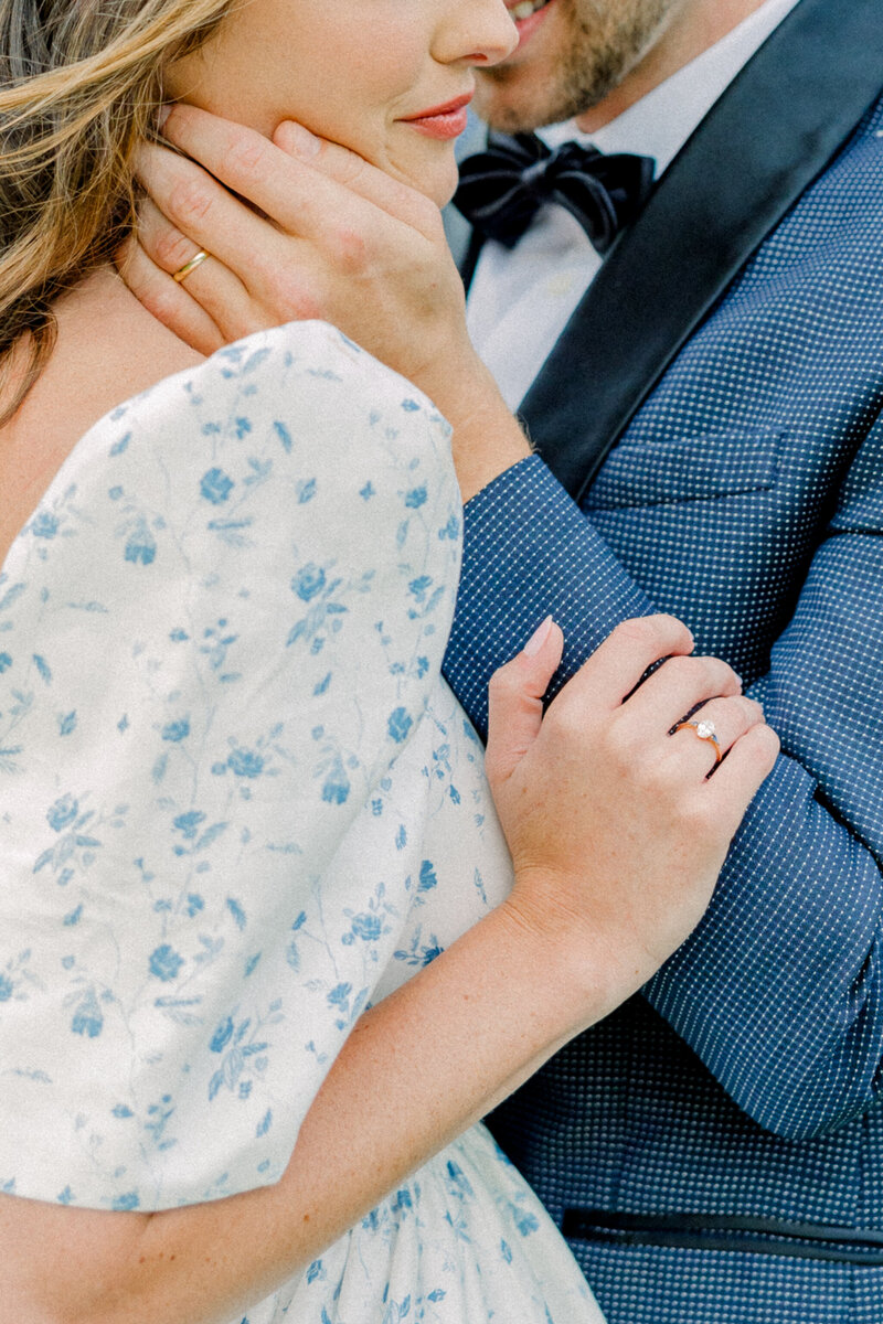Ivy Rose Barn | A closeup romantic and editorial image of a bride and groom holding each other. The bride wears a vintage-inspired floral gown with puff sleeves, while the groom is in a navy tuxedo. Their embrace shows both of their gold wedding rings.