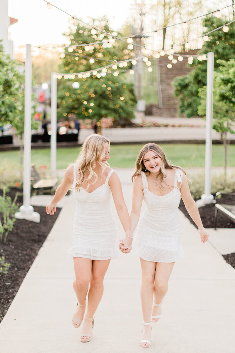 Two girls in white dresses holding hands and posing for senior photos
