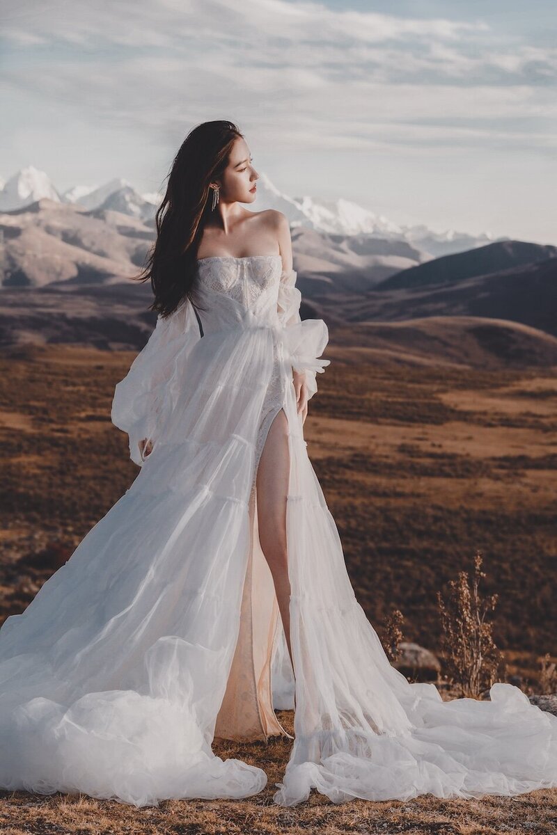 A bride photographed in the golden evening light in a wild field with. mountains in the background.