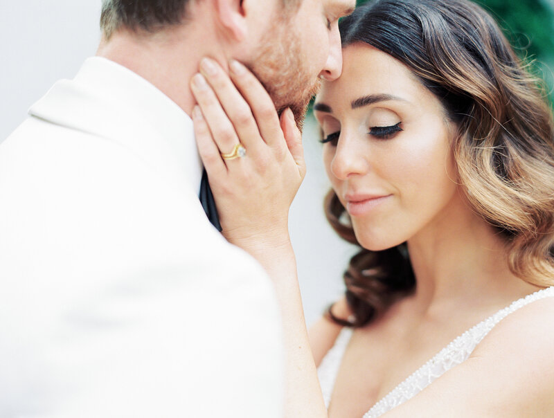 bride with her hand  on the grooms face and she's looking down