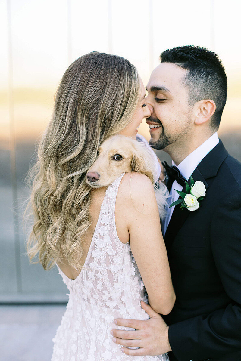 A bride and groom share an intimate moment while holding their small dog between them at SoHo63, a Chandler wedding and event venue. The bride’s lace gown and the groom’s boutonnière add elegance to this tender, pet-friendly wedding day portrait.