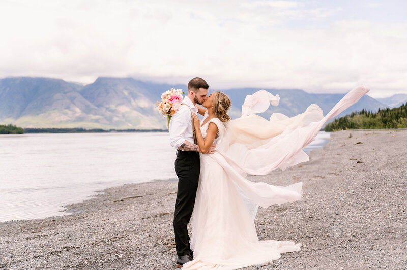 bride and groom kissing with Alaskan mountains and lake in the background