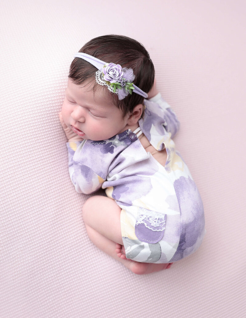 Adorable newborn baby girl wearing a floral outfit, peacefully sleeping at a photography studio in Rochester, NY.