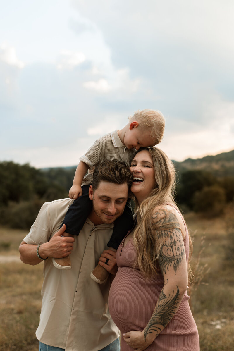 Pregnant woman and husband holding toddler boy on dad's shoulders