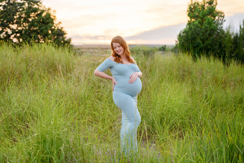 red-haired pregnant woman standing in grass with the sunsetting behind her for her outdoor maternity photography session Burlington, Ontario.