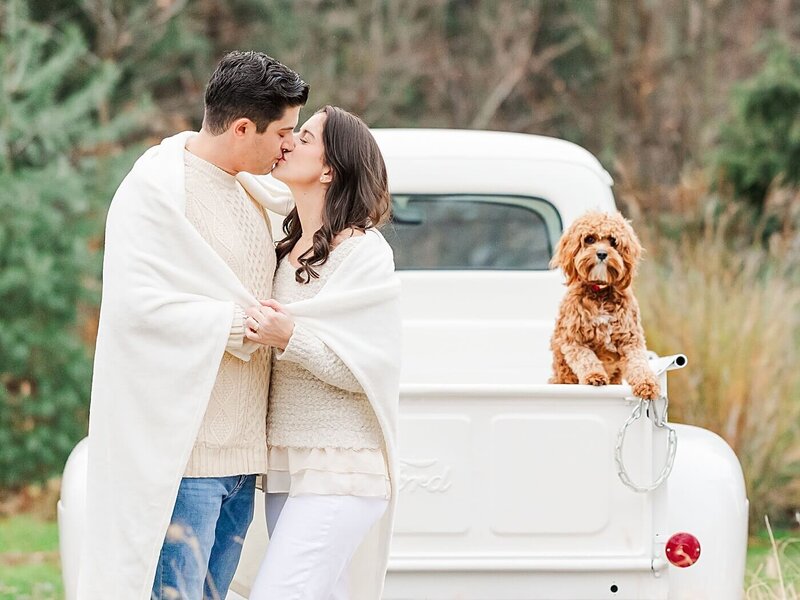 Husband and wife kissing with their dog in a truck for Christmas photos.