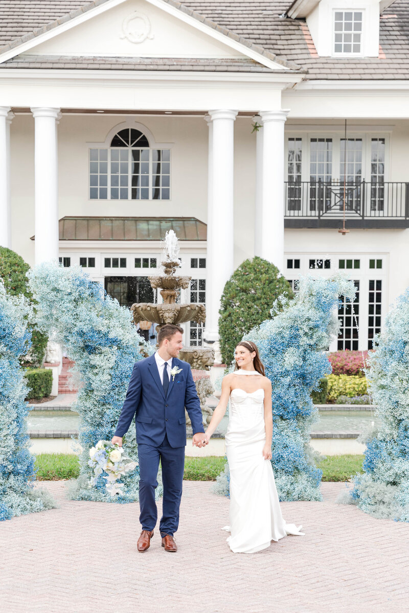 Florida wedding venue Luxmore Grande Estate with bride and groom posing by grand entrance and blue florals