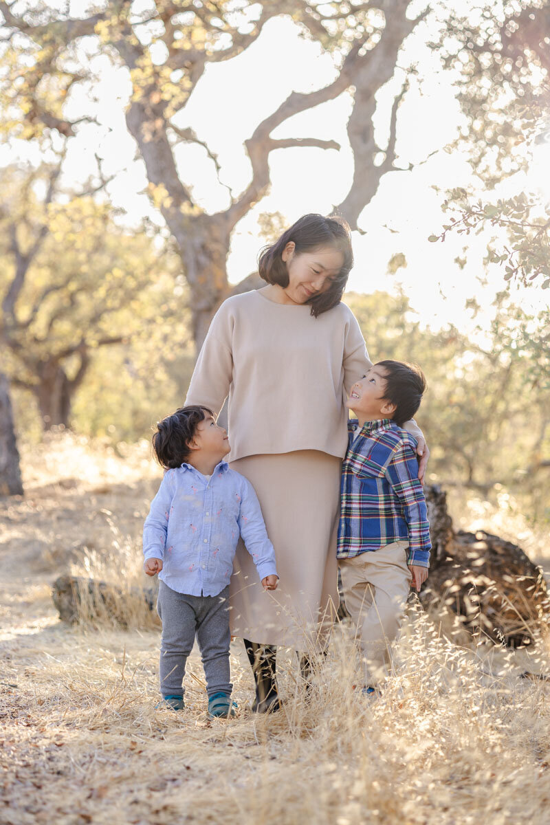 Mother gazing lovingly down at her two young sons who look up at her during golden hour family session in San Jose