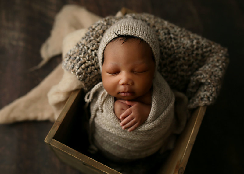 newborn in neutral toned wraps in wooden box prop