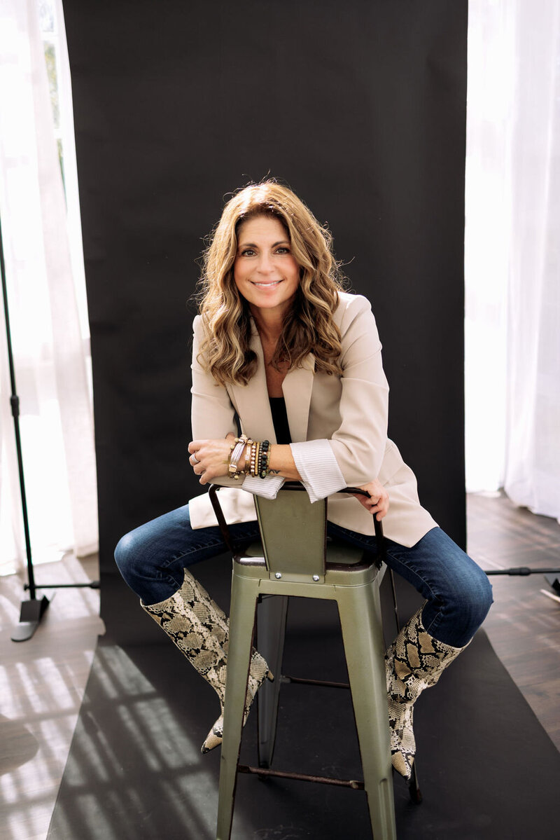 Kerri Link sits in a bright studio, smiling confidently and reflecting her grounded, compassionate energy as a coach.