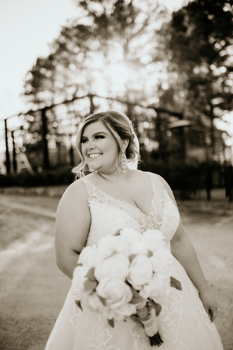 little rock wedding photographers capture outdoor bridal portraits with bride in a lace wedding gwon holding her wedding bouquet and smiling to the side