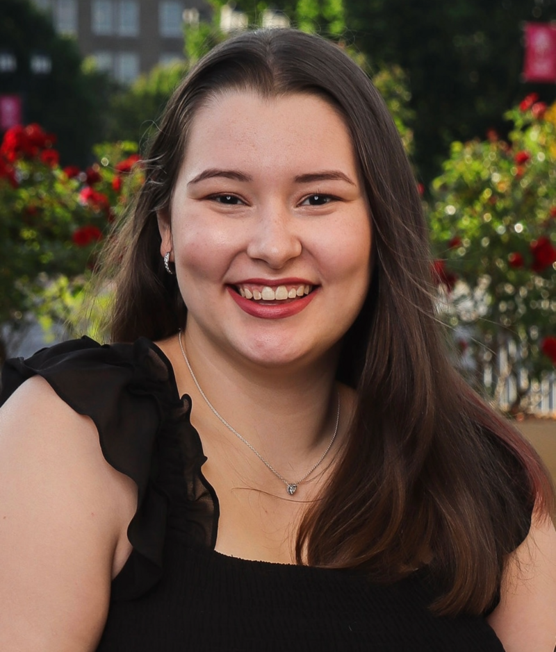 Aubrey is a smiling young white woman with long straight brown hair, dark brown eyes. She is wearing a sleeveless black blouse with frilly shoulder straps.