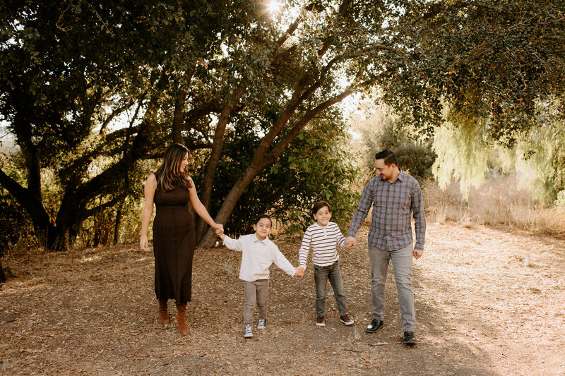 Family of four holding hands and walking together during a relaxed fall family photo session  at Horse Thief Canyon Park in San Dimas, California. 