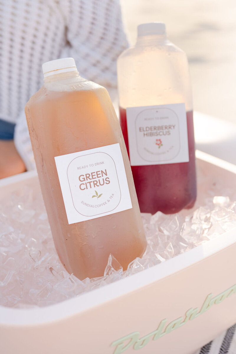 half gallon jugs of sundial iced teas on ice in a cooler sitting on the beach in surf city