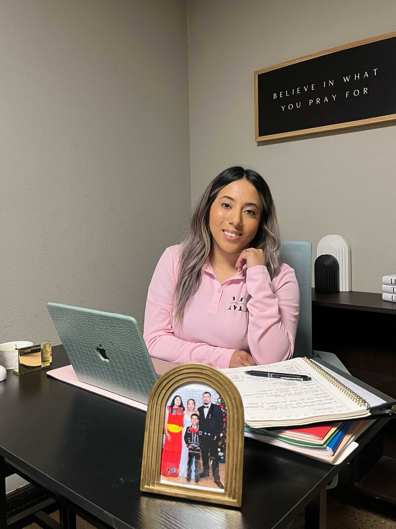 Full-service residential and commercial renovations professional sitting at her office desk with important documents in front of her. A family portrait on the desk reflects the importance of family values in her business.