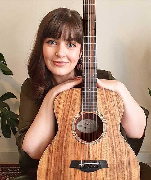 Portrait of female guitarist smiling warmly while holding a Taylor acoustic guitar, used for Coldplay acoustic sessions