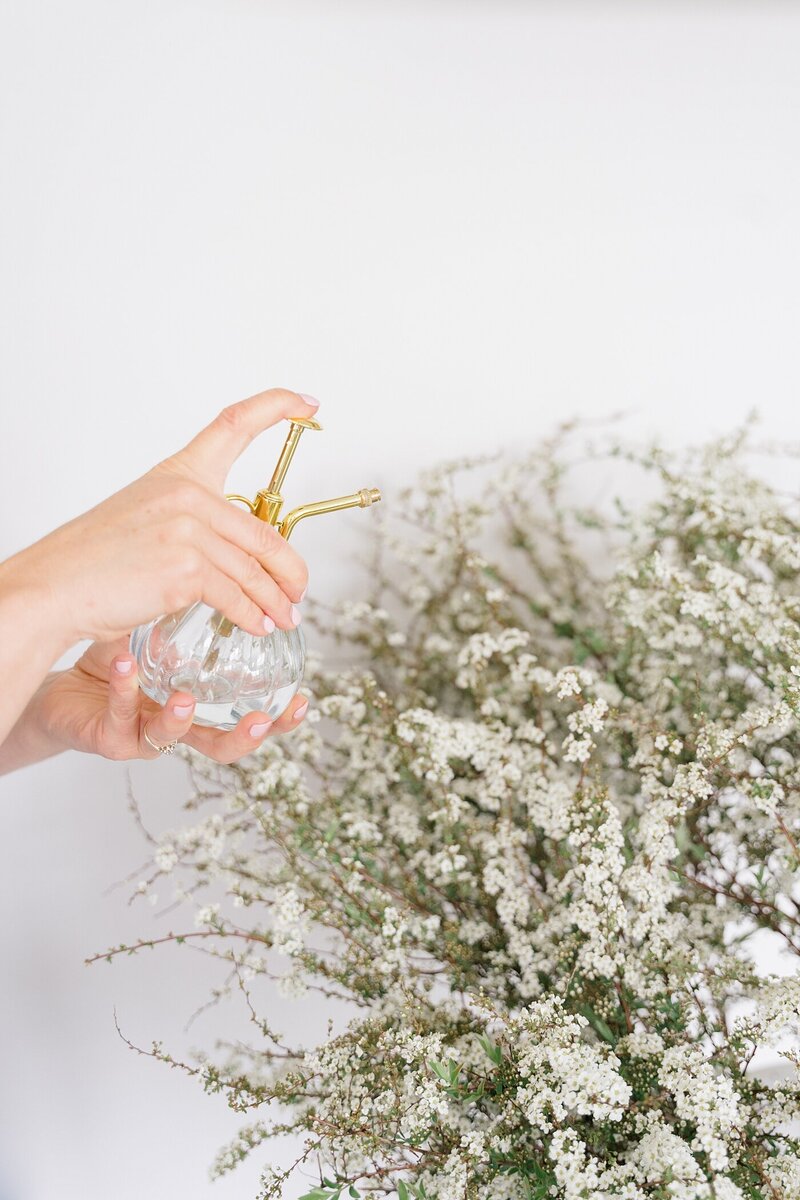 product photography with person holding a spray bottle and spraying white florals  photographed by Columbus photographer