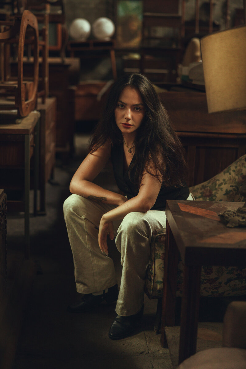 Utah creative portrait of woman sitting on antique chair. Elbows on knees. Looking at the camera with a straight face.