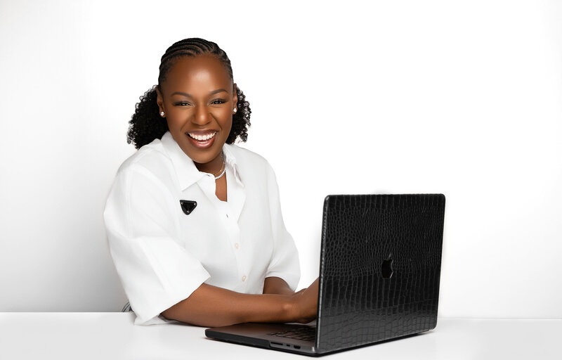 Rianne Nycole, a smiling Black woman with braided hair, sitting at a desk with a laptop, wearing a white blouse and statement brooch. The background features bold, circular branding elements in purple and gold.
