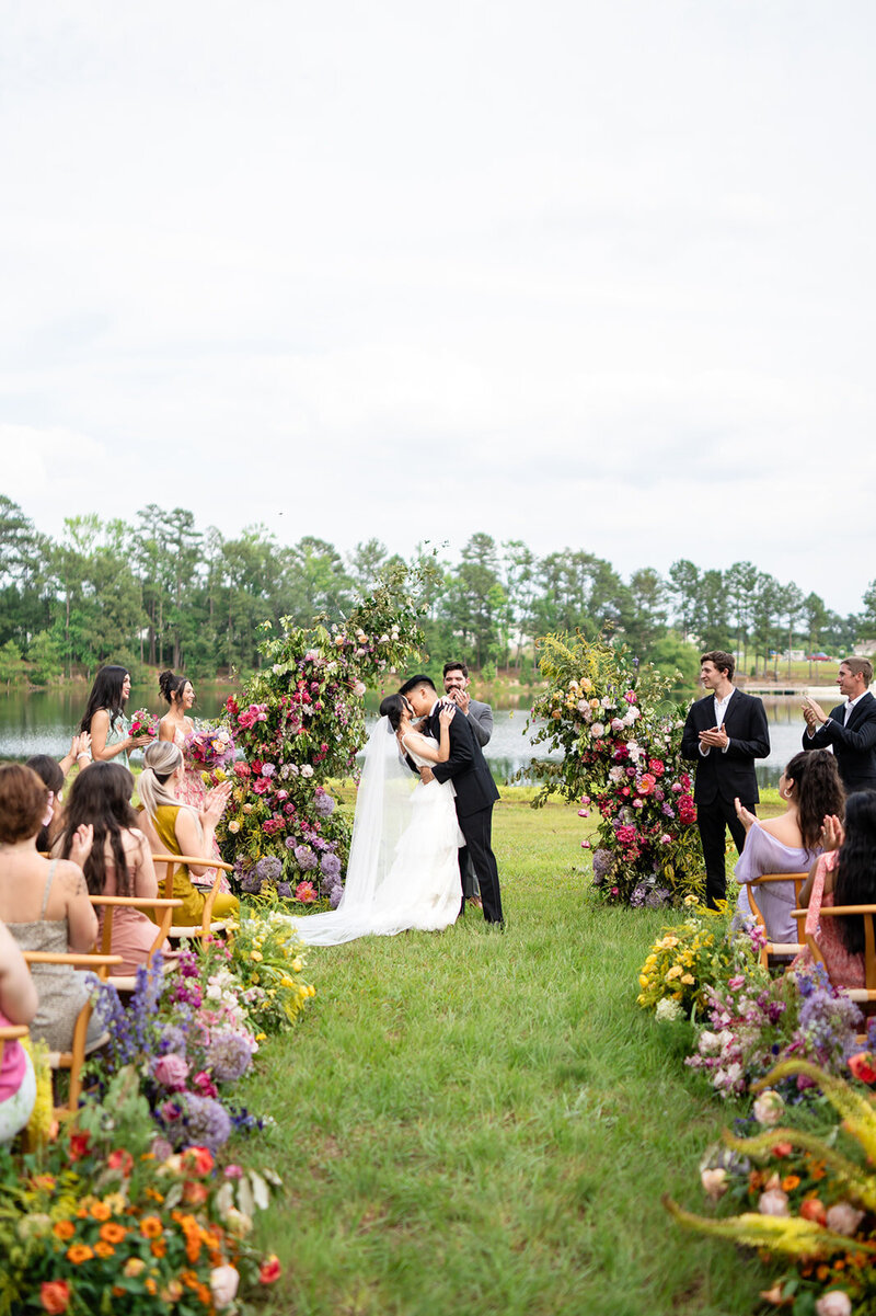 Bride and groom share their first kiss under a vibrant floral arch
