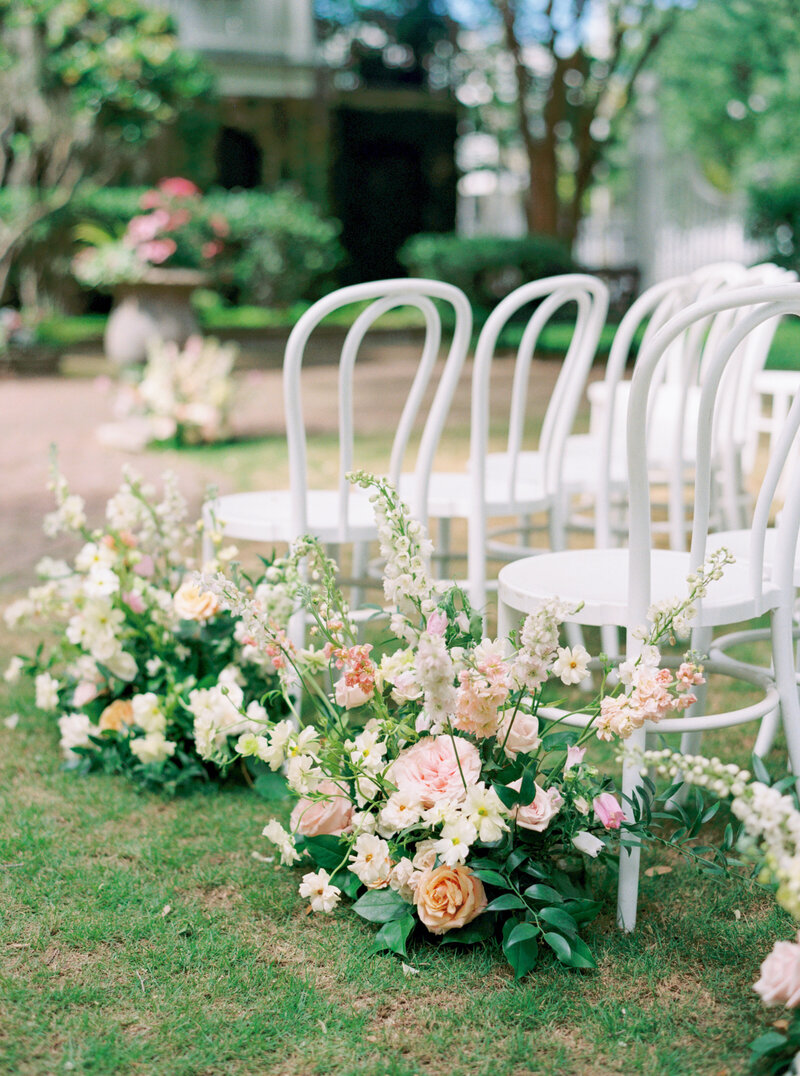 White ceremony chairs with pale pastel flowers lining the aisle.