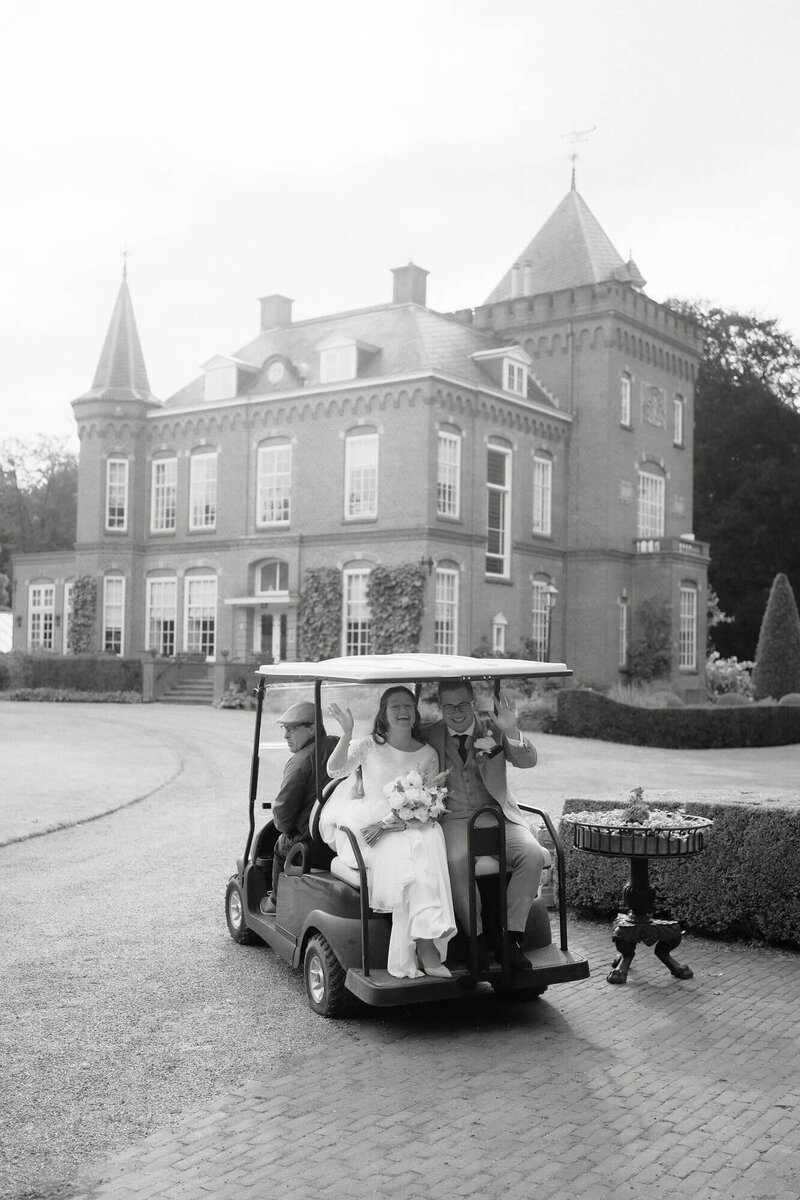 Een bruid en bruidegom in een golfkar voor kasteel, gefotografeerd door trouwfotograaf Julia de Groot
