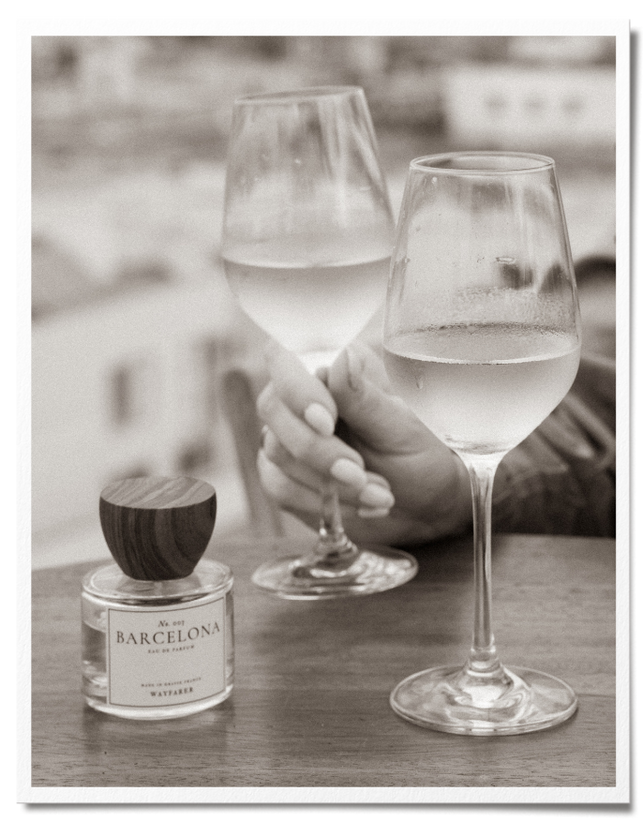 Perfume bottle on table with woman holding wine glasses on a  Barcelona rooftop