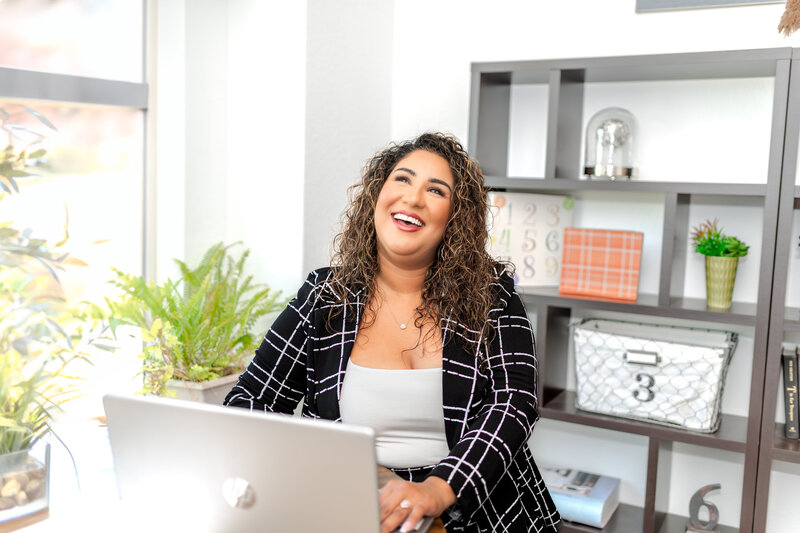 New Braunfels realtor sitting in front of laptop, smiling and looking away from camera during branding session.