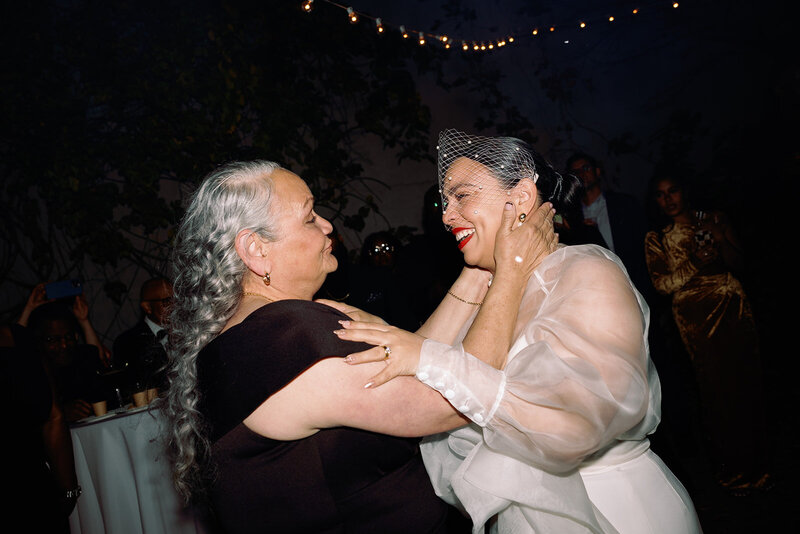 bride and her mom holding eachothers faces smiling at wedding