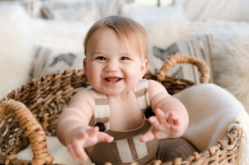 Ten month old baby boy reaching toward camera smiling in natural basket with neutral tones - milestone photography by Glean and Co Boise studio
