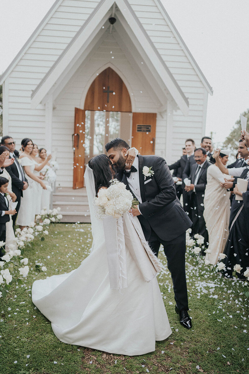 couple just married in front of their chapel with long veil which has their names and wedding date engraved, white roses surround them