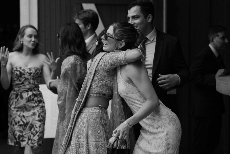 Two people hug as wedding guests talk behind them 