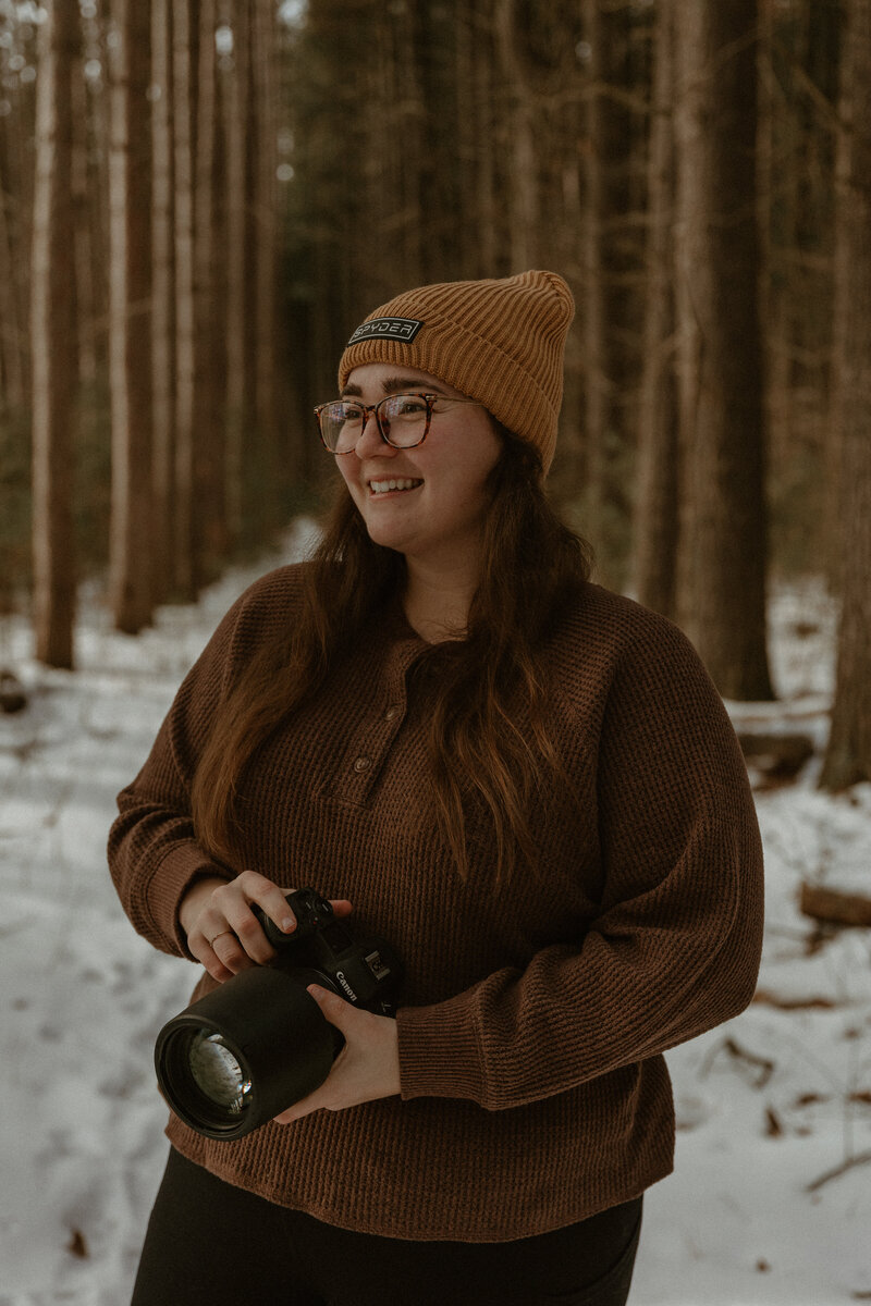 A photo of a girl holding a camera smiling in the woods