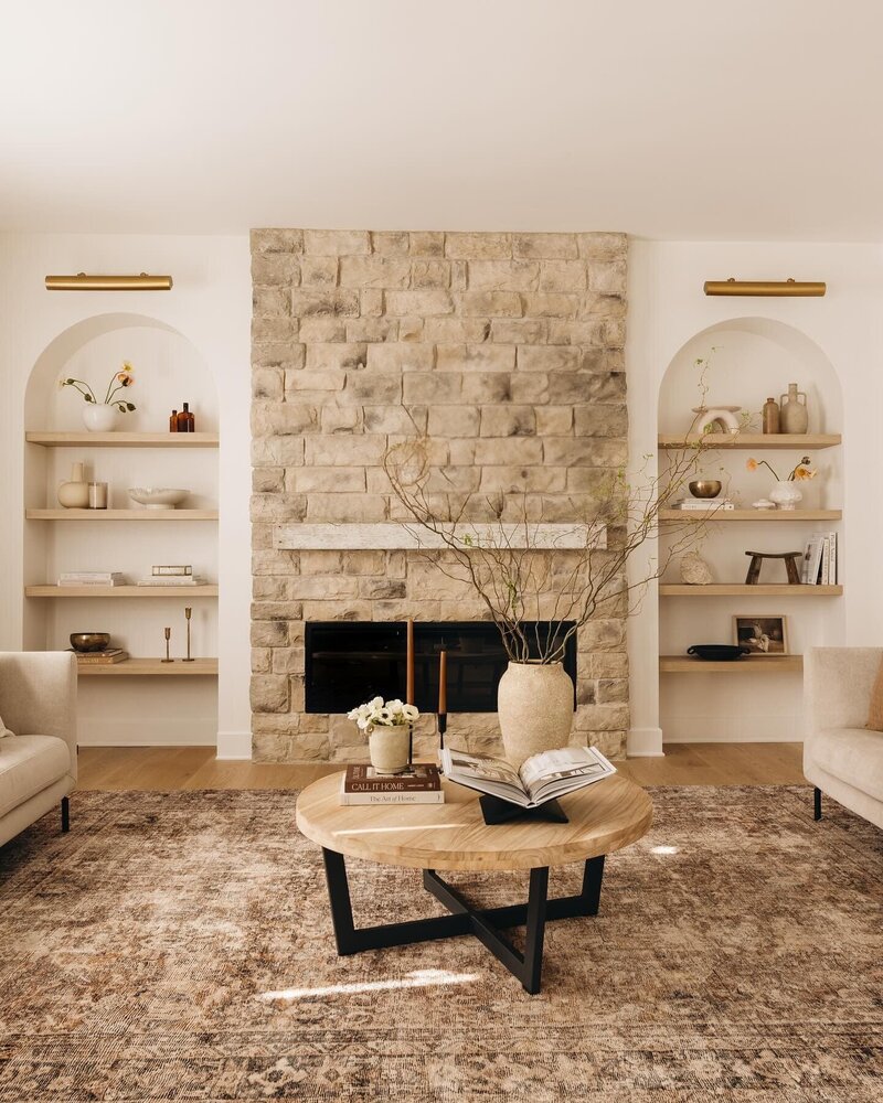Organic modern living room in Montreal with a stone fireplace, neutral-toned furniture, and arched built-in shelves – by Ingrid Interior Design.